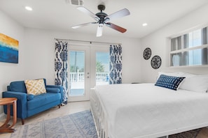 A bedroom with a bed, a blue sofa, a ceiling fan, and a view through the glass door.