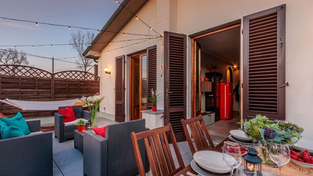 An outdoor patio with wicker furniture, a dining table set for two, and string lights.