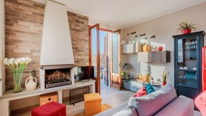 A modern living room with a fireplace, a sofa, and a coffee table. There is a brick wall and a wooden door leading to another room.
