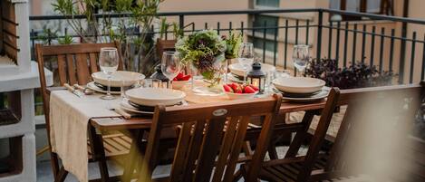 A dining table set outdoors with wooden chairs, plates, glasses, and a centerpiece of flowers and strawberries.