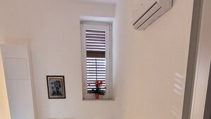 A living room with a sofa, a dining table with chairs, a window with blinds, and a small plant. - Housestation suite H (Palermo)