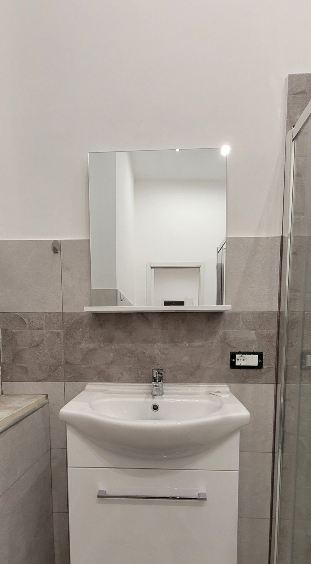 A bathroom with a white sink, a mirror above it, and a shower area to the right.