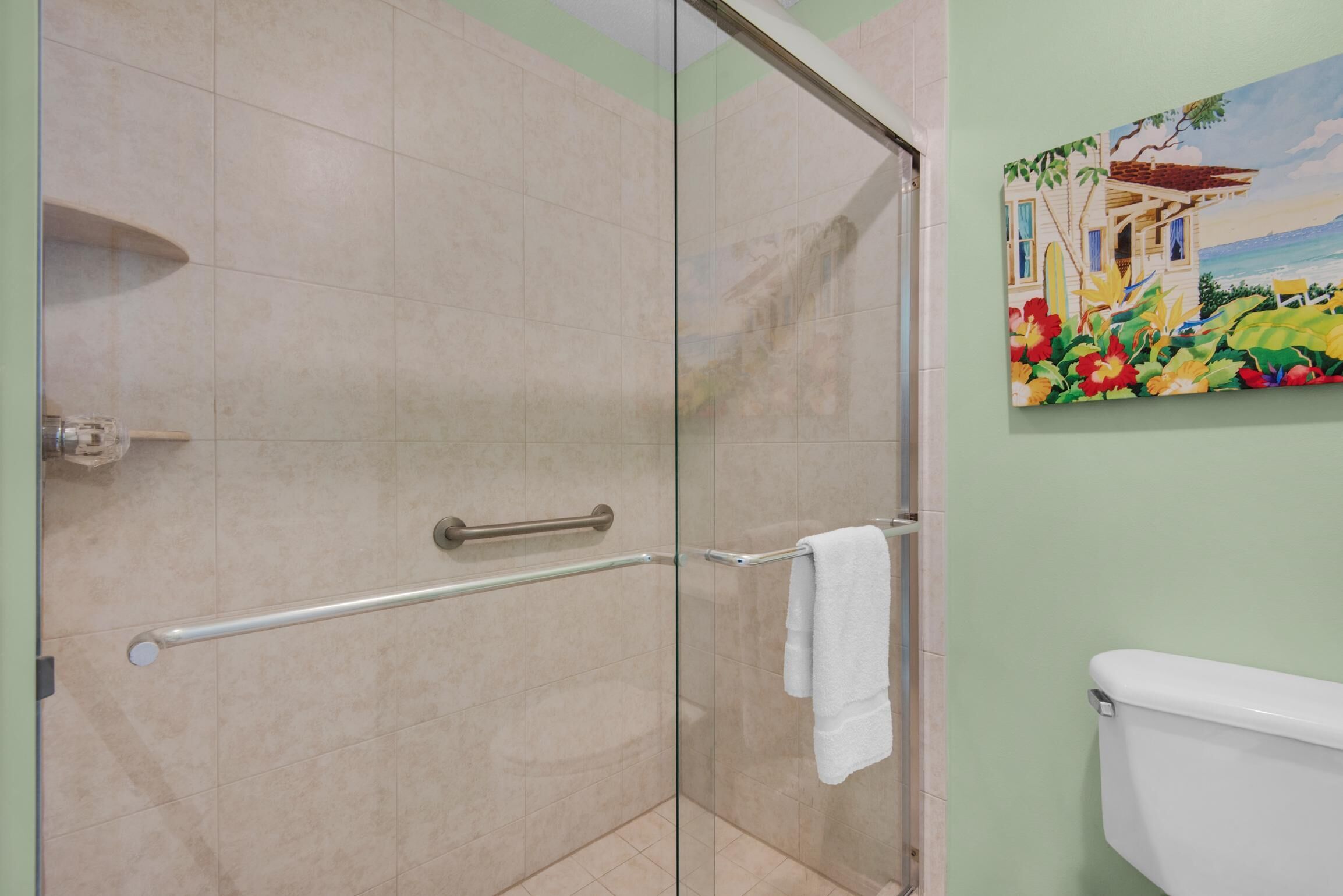 A glass-enclosed shower with a handrail and a white towel hanging on the wall.