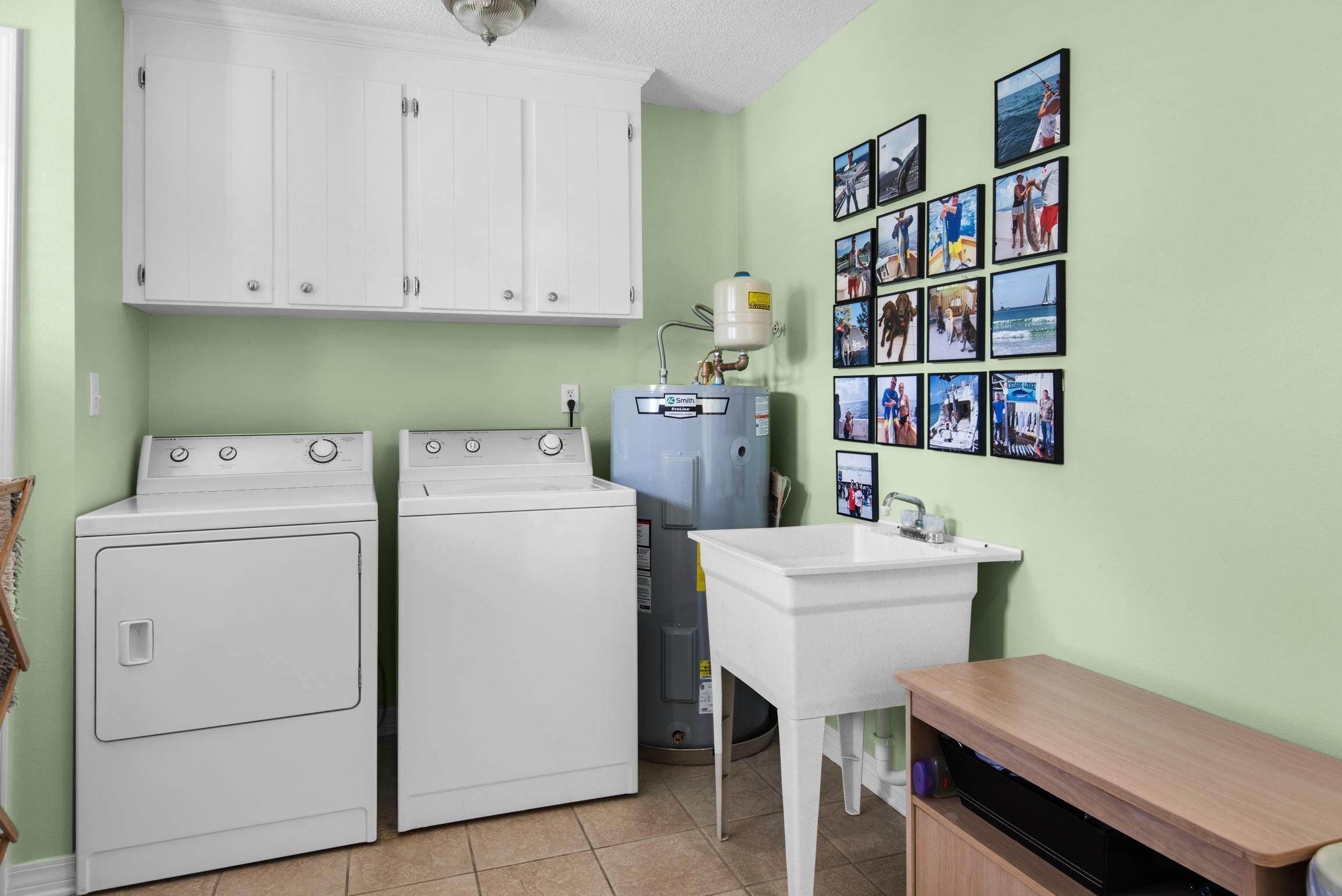 A laundry room with two white washers and dryers, a water heater, and a sink.