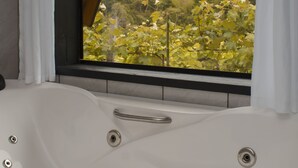 A modern bathroom with a large bathtub, a window with a view of a green landscape, and a wooden ceiling. - Refúgio do Vale Cabanas Exclusivas (Bento Gonçalves)