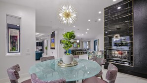 A modern dining area with a glass table, patterned chairs, and a central plant. - Rising Sun House: Pool, Spa, GameRoom, PetFriendly! (Palm Springs)