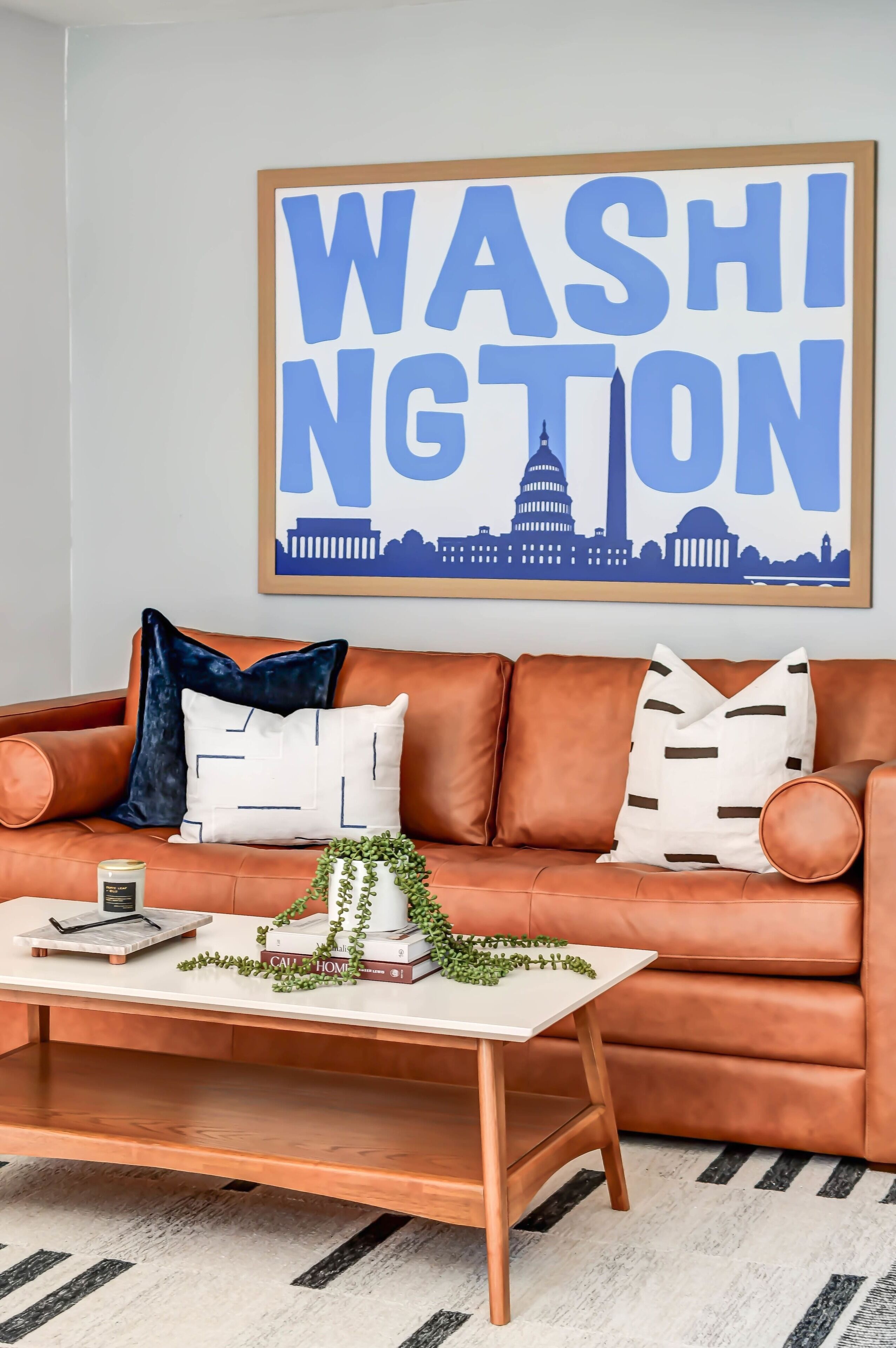 Un salón con un sofá de cuero marrón, una mesita de centro blanca y un cartel enmarcado que dice 'Washington'.