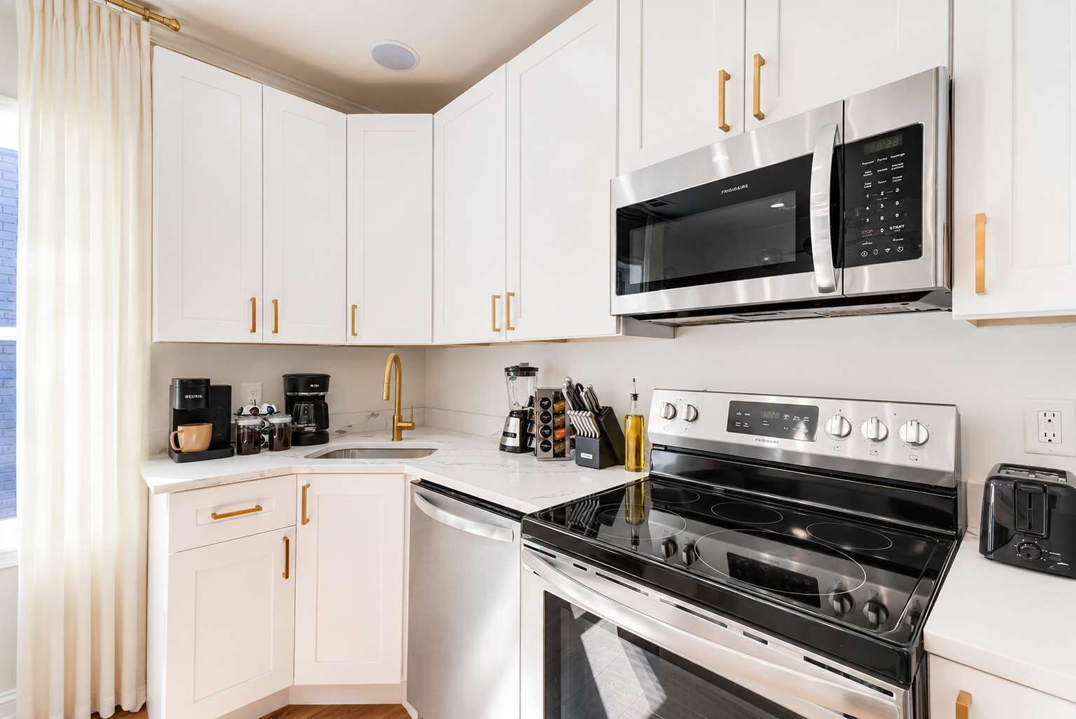 A modern kitchen with white cabinets, a stainless steel range, a microwave, a dishwasher, and a toaster.