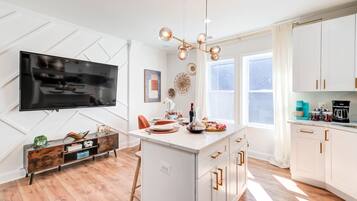 Een moderne keuken met een centraal eiland, witte kasten, een flatscreen televisie en een hanglamp.