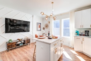 A modern kitchen with a central island, white cabinetry, a flat-screen TV, and a pendant light.