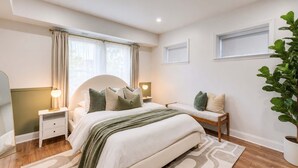Ein Schlafzimmer mit Bett, Nachttischen, einer Lampe, einem Blumentopf und einem Fenster.