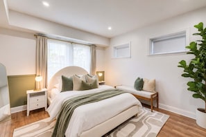 A bedroom with a bed, bedside tables, a nightstand, a lamp, a potted plant, and a window. - Lincoln Lofts: 201 | 2BR Sunlit Designer Retreat (Washington)