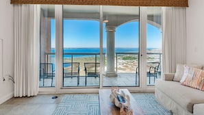 A spacious living room with a large sliding glass door leading to a balcony with a view of the beach.