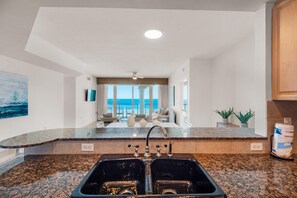 Cozinha com bancadas de granito, uma pia dupla e vista para o oceano através de grandes janelas.