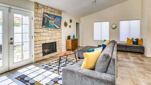 Una sala de estar con chimenea de piedra, un sofá gris y un tapete estampado.
