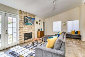 Un salon avec une cheminée en pierre, un canapé gris et un tapis à motifs.
