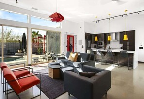 Una sala moderna con un sofá, sillas y un comedor con cocina al fondo.