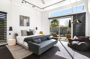 Un dormitorio moderno con cama, sofá gris y un ventanal grande.