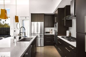 Una cocina moderna con electrodomésticos de acero inoxidable, armarios oscuros y una isla grande con fregadero.