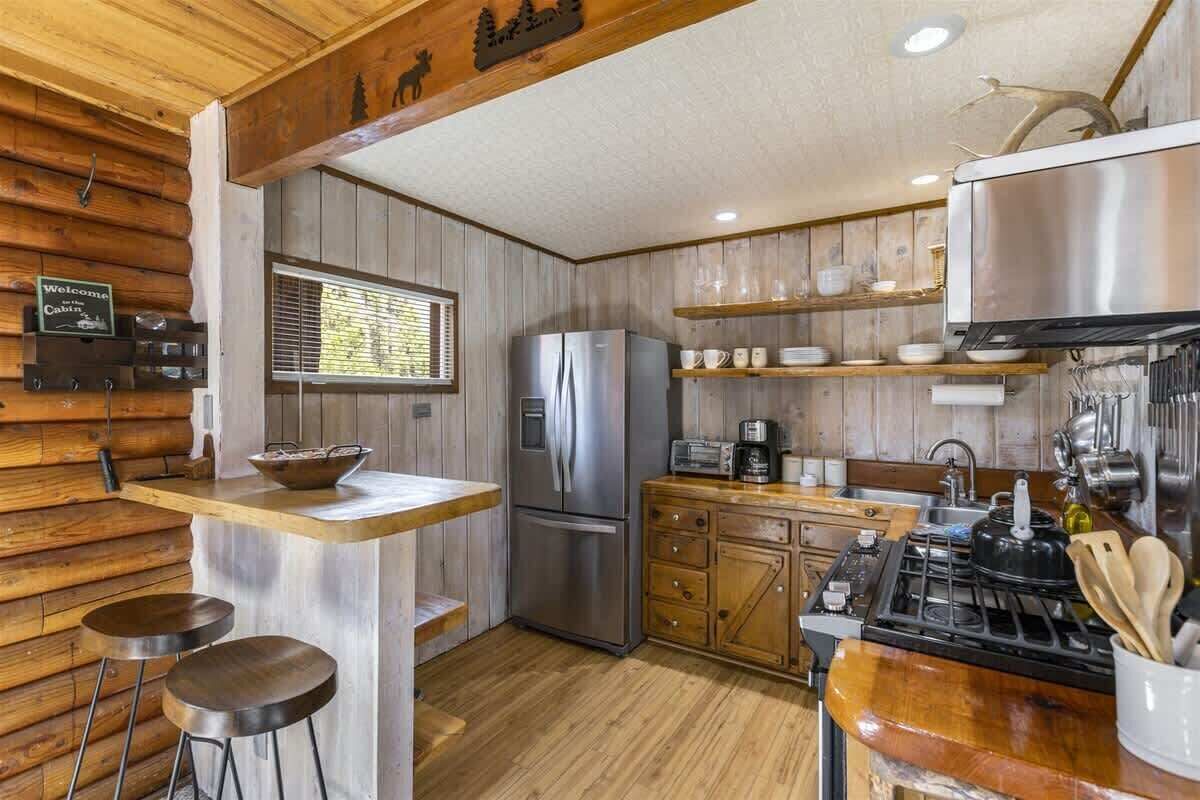 Een keuken in chaletstijl met een houten inrichting, een roestvrijstalen koelkast, een fornuis en barstoelen.