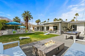 Une terrasse extérieure moderne, dotée d’une table de billard, de fauteuils et d’un foyer.