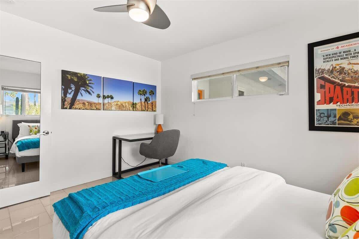 Une chambre d’hôtel avec un lit, un bureau, une chaise, une fenêtre et des œuvres d’art accrochées au mur.