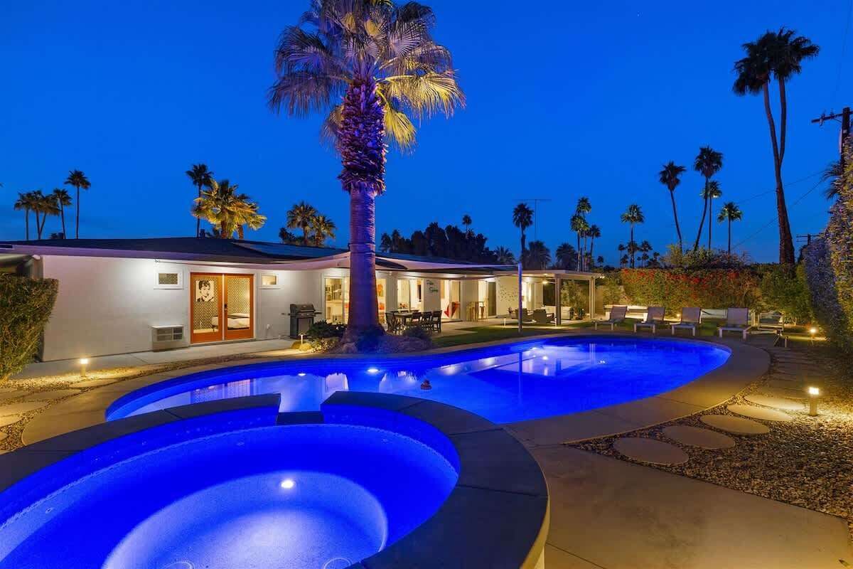 Une piscine au design incurvé, un palmier et un bâtiment doté d’une porte et de fenêtres.