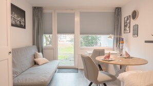 Una habitación moderna con sofá, una mesa de comedor con sillas, una ventana con persianas y vistas al exterior.