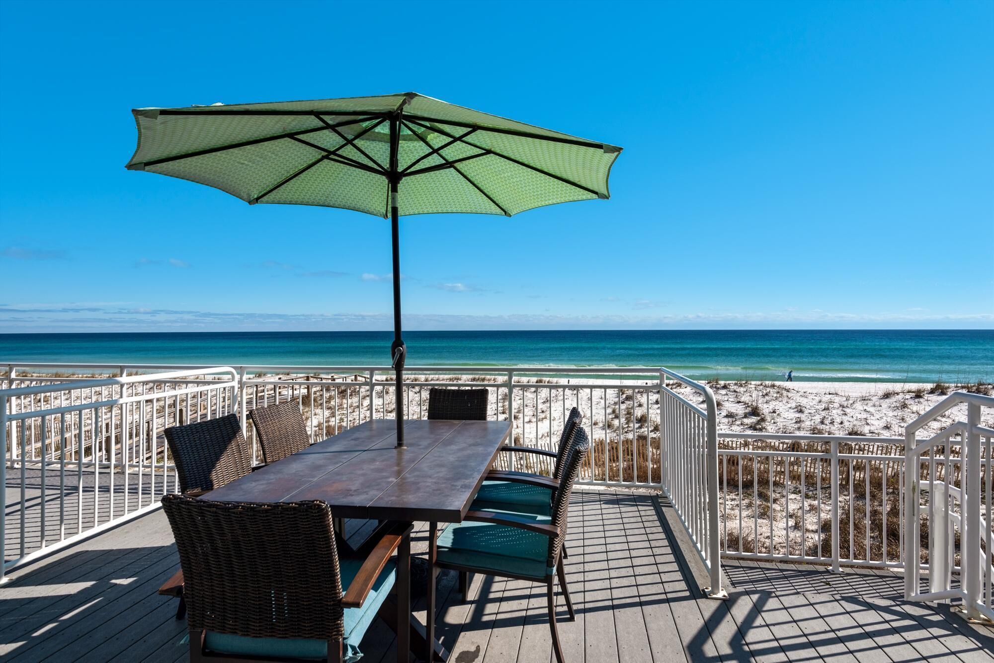 Una terraza con mesa y sillas, una sombrilla y vistas a la playa y al océano.