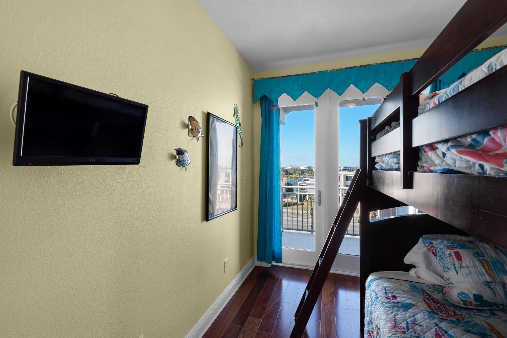 A room with a bunk bed, a flat-screen TV mounted on the wall, and a window with a view of buildings.