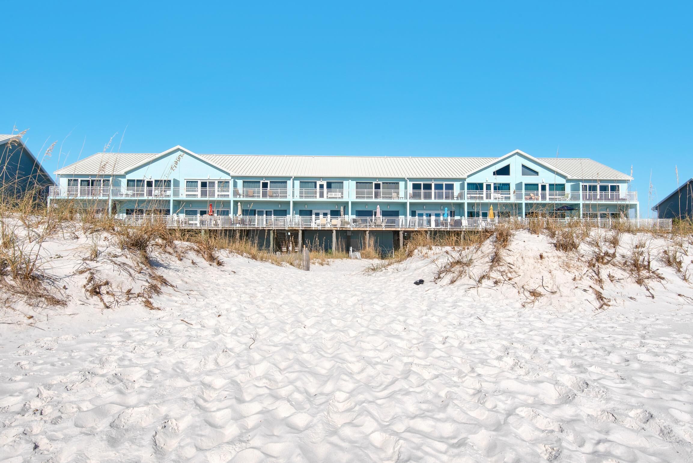 Un hotel frente a la playa con fachada azul claro, varios balcones y una playa de arena en primer plano.