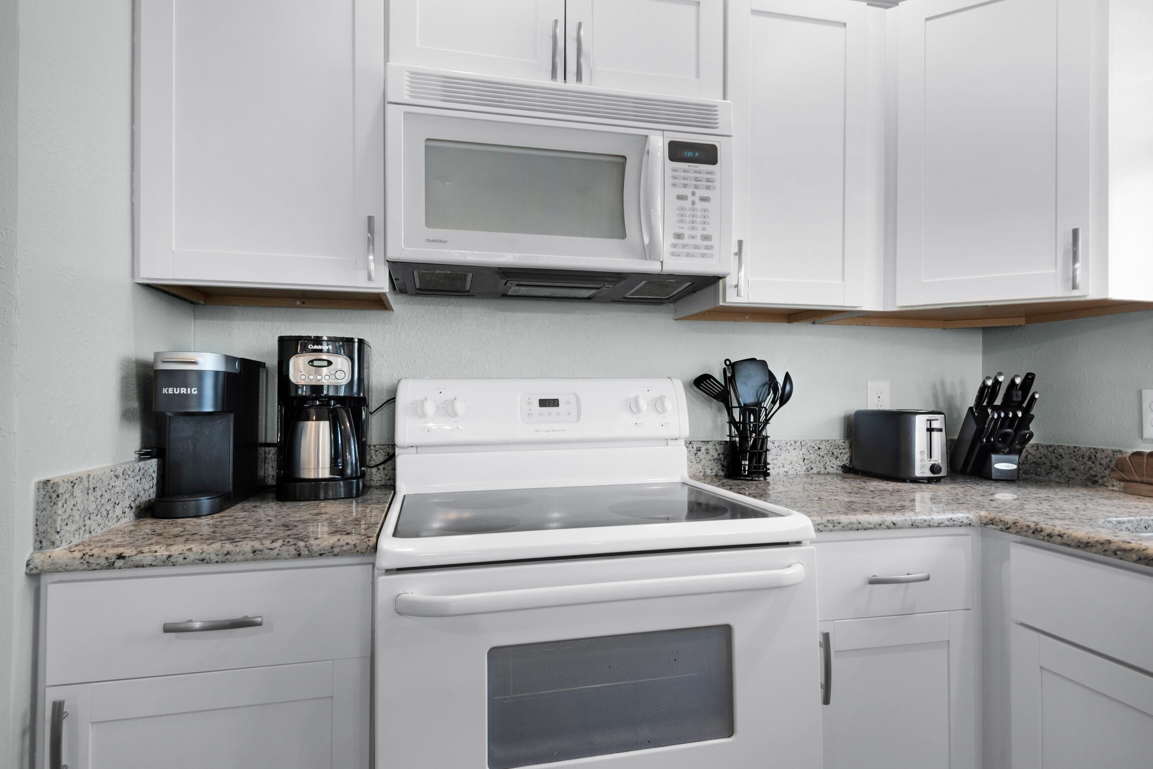 A kitchen with white cabinets, a microwave, a coffee maker, a toaster, and a stove.