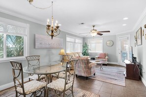A dining area with a glass table and chairs, a chandelier, ceiling fan, and a painting on the wall. - Sunset Harbor Palms 2-301 (Navarre)