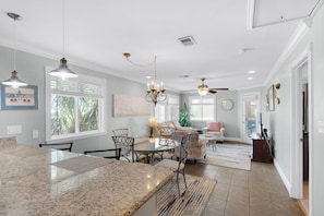 A spacious kitchen with granite countertops, a dining area with a table and chairs, a living room with a sofa and a coffee table, and a ceiling fan. - Sunset Harbor Palms 2-301 (Navarre)