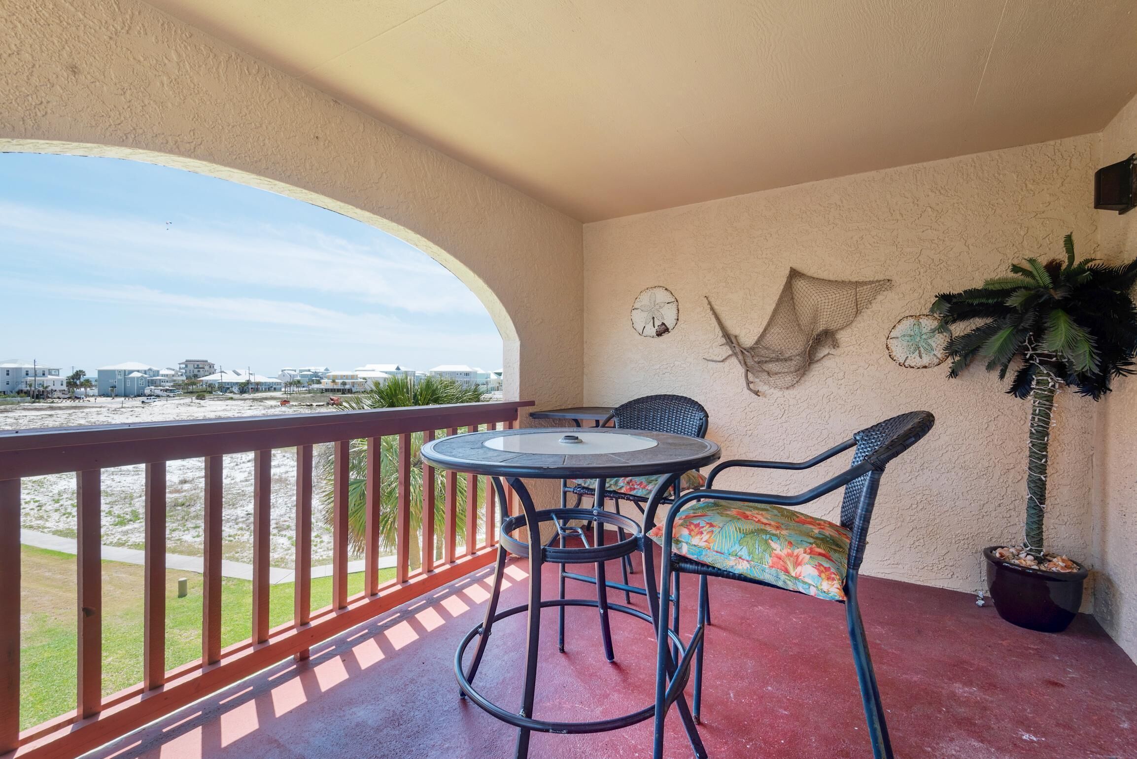 Un balcon avec une table ronde et des chaises, un pot de fleurs et une vue sur la plage.
