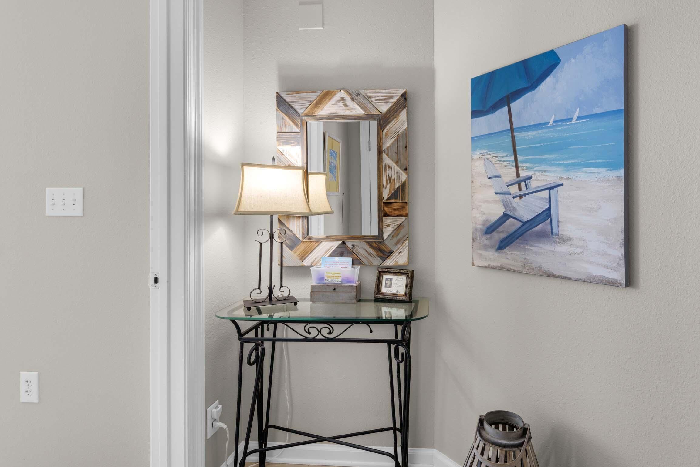 A corner with a glass-top table, a lamp, a framed photo, and a beach painting.