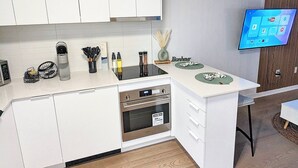 Une cuisine moderne avec des meubles blancs, un four encastré et un téléviseur à écran plat fixé au mur.