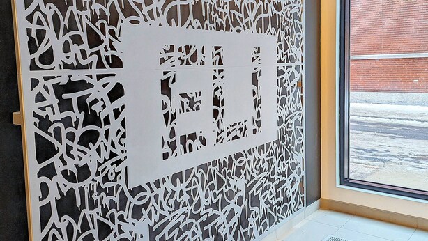 Un intérieur moderne agrémenté d’un mur décoratif orné de motifs complexes découpés, et d’une grande fenêtre offrant une vue sur l’extérieur.