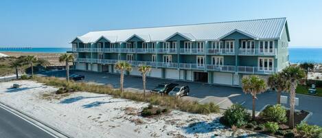A beachfront hotel with multiple balconies, a parking lot, and a view of the ocean.