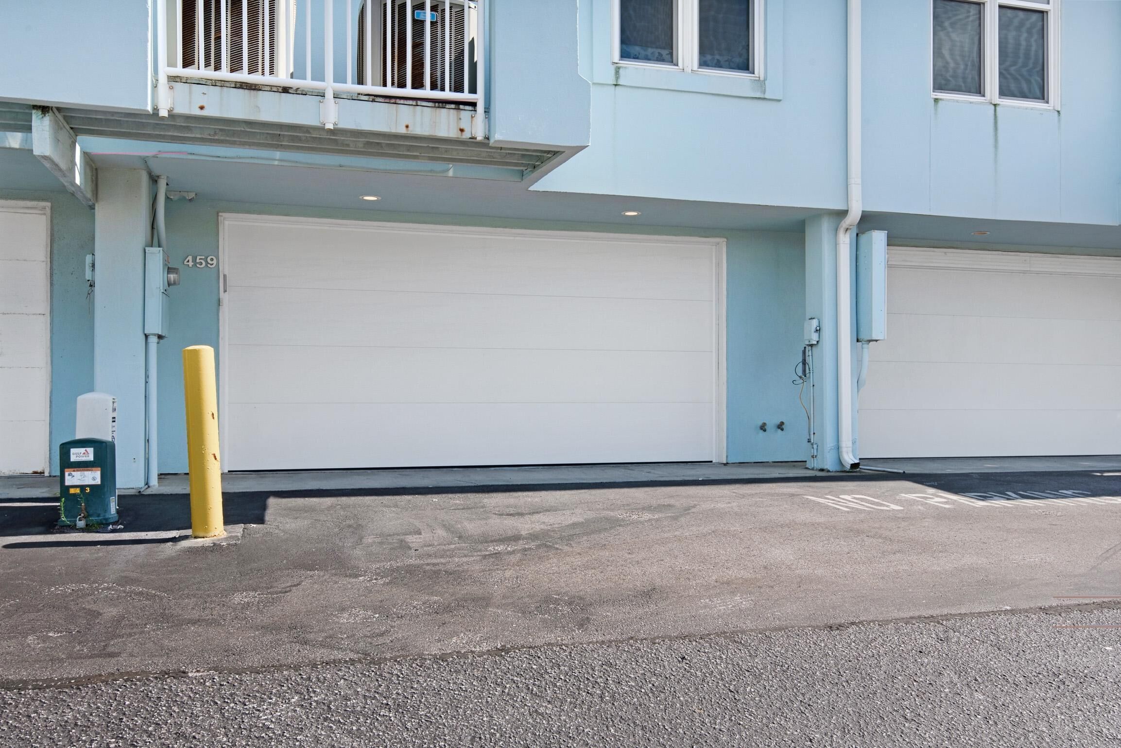 A building with two garage doors, a yellow bollard, and a trash can.