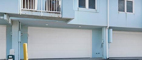 A building with two garage doors, a yellow bollard, and a trash can.
