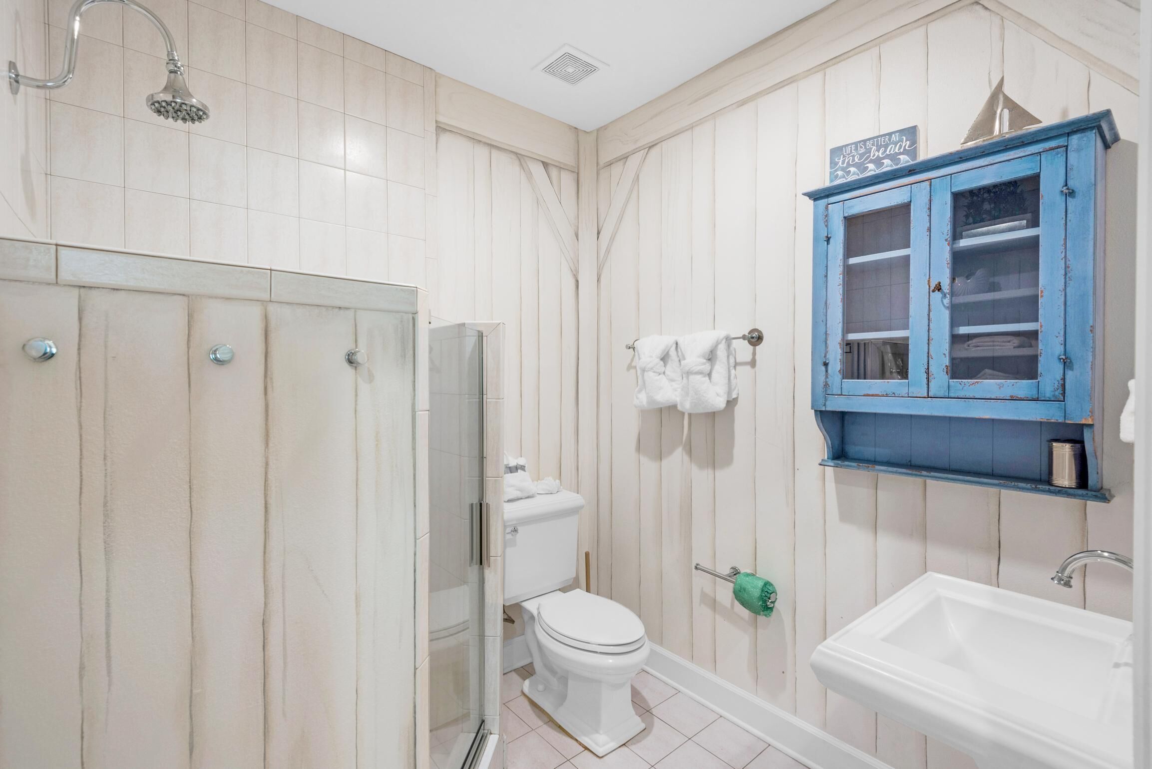 Een badkamer met douche, toilet, wastafel en een blauwe kast met glazen deuren.