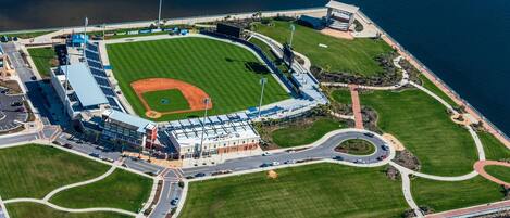 Vista aérea de un estadio de béisbol con un amplio campo, zonas de asientos y un estacionamiento.