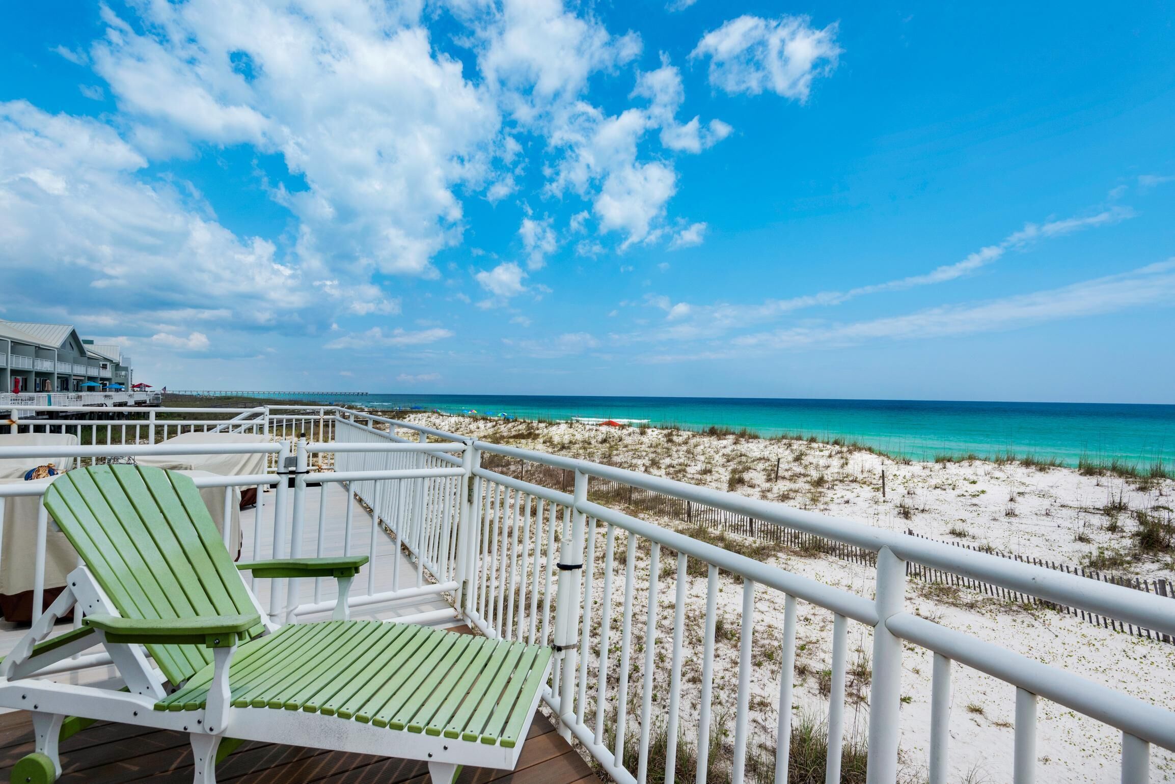 Eine Terrasse mit grünen Stühlen und einem Tisch mit Blick auf einen Strand mit weißem Sand und türkisblauem Wasser.