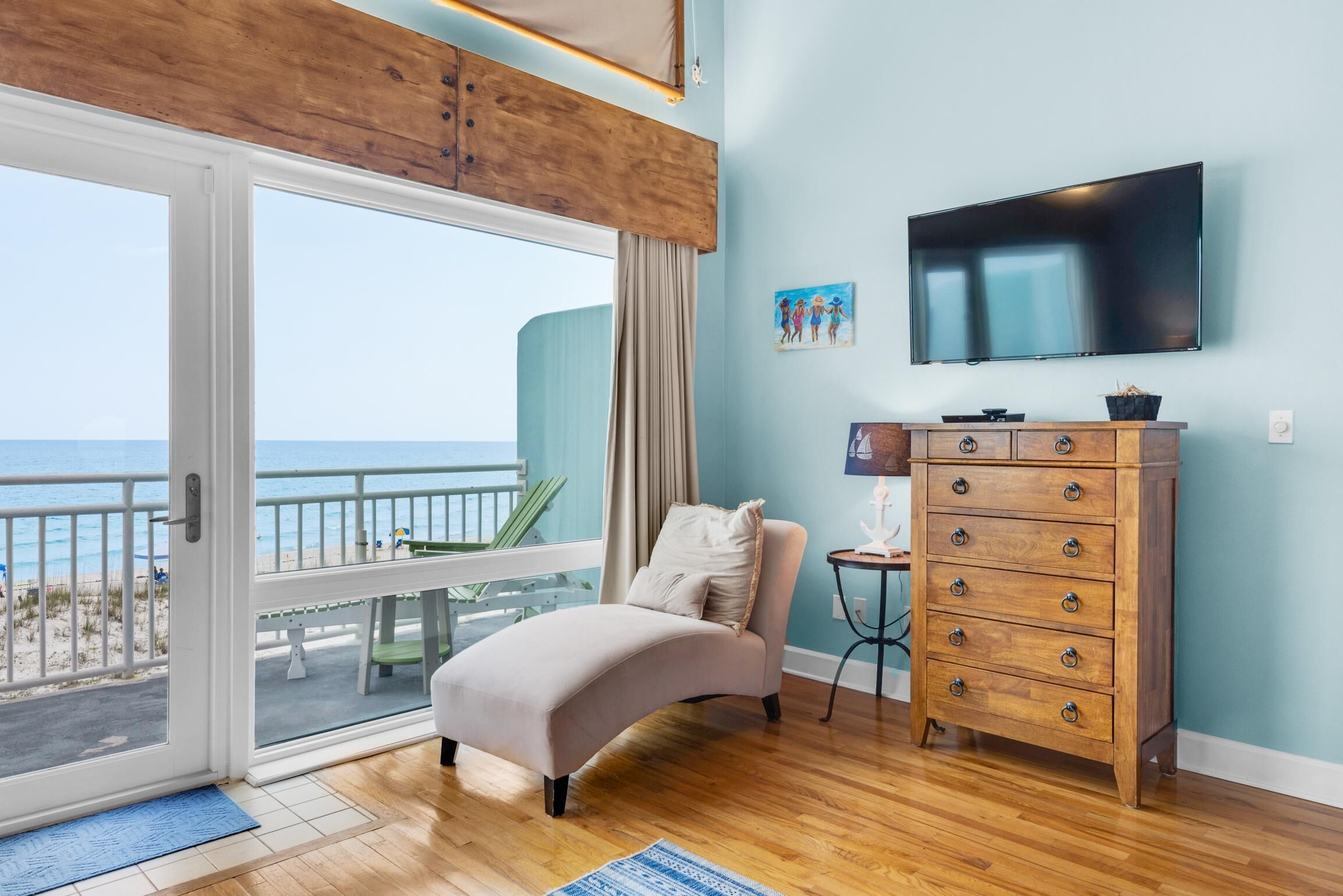 A bedroom with a large sliding glass door leading to a balcony, a bed, a wooden dresser, and a flat-screen TV mounted on the wall.