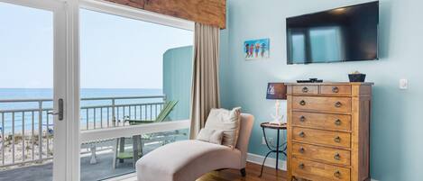 A bedroom with a large sliding glass door leading to a balcony, a bed, a wooden dresser, and a flat-screen TV mounted on the wall.