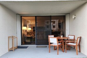 Ein Balkon mit Glastür, Holzstühlen, einem kleinen Tisch und einer Lampe.