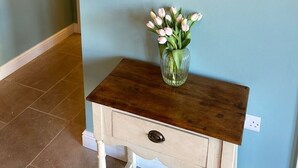 A hallway with a round mirror on the wall, a small wooden console table with a vase of flowers, and a framed picture on the wall. - A family and dog friendly haven, The Hayloft. (Sweffling)