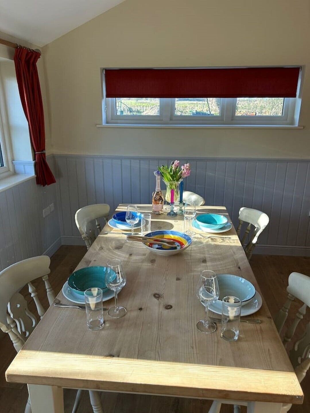 Une table à manger avec de la vaisselle bleue et transparente, une bouteille et un vase rempli de fleurs.
