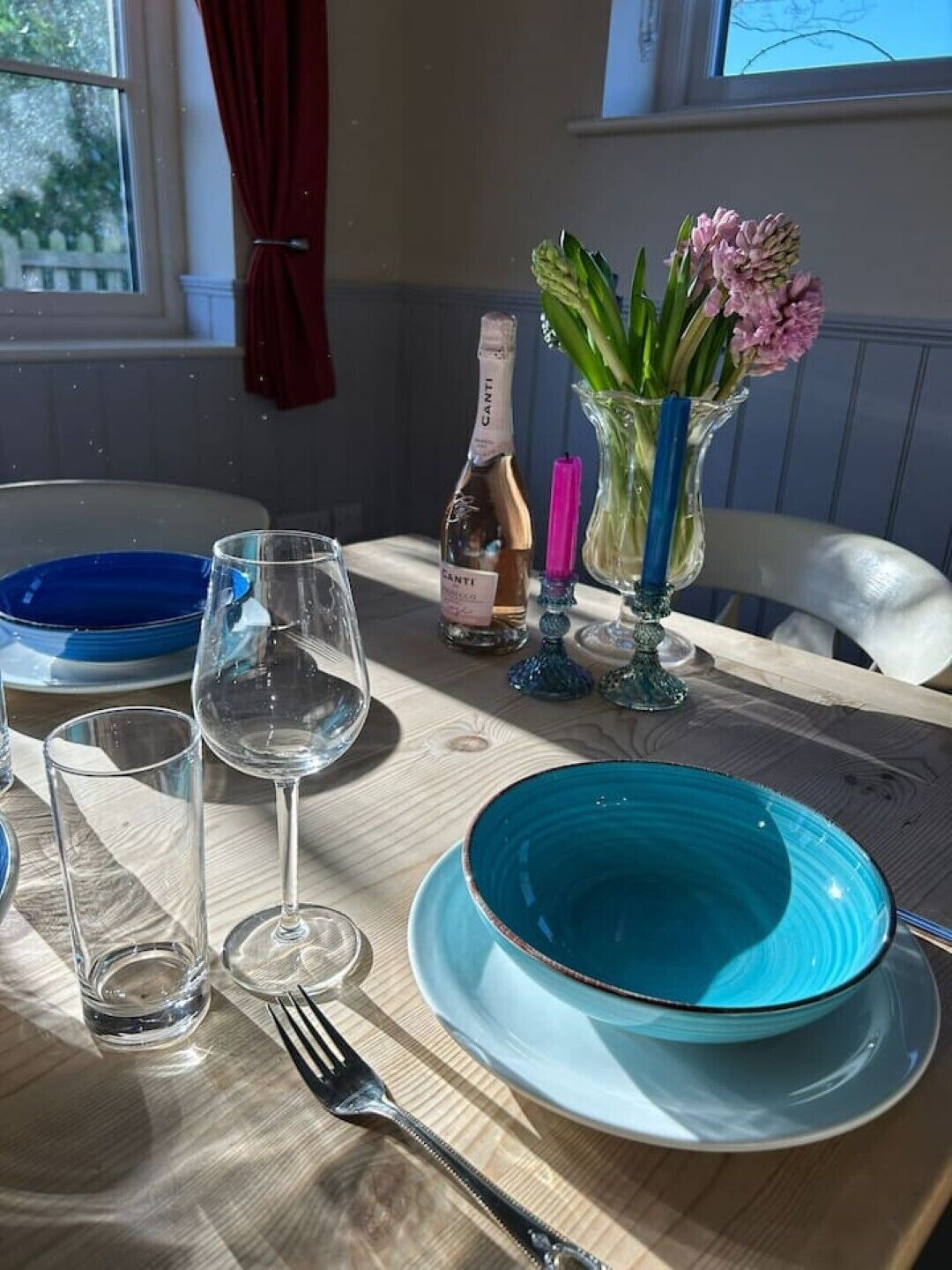 A dining table set with blue plates, wine glasses, and a bottle of Canti wine.